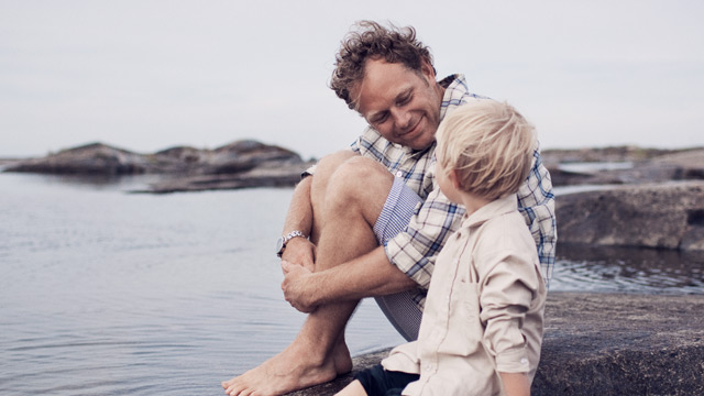 Dad and son smiling by the sea during summertime.