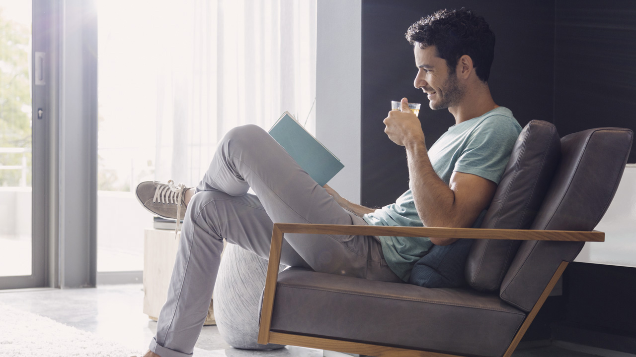 Man sitting in armchair drinking coffee reading