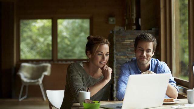 Par hjemme som smiler og spiser foran laptop.