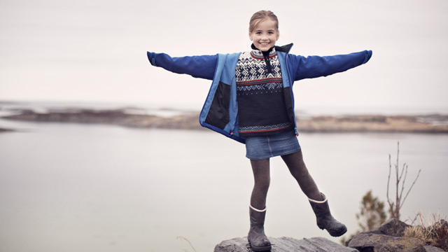 A kid is smiling on a rock by the sea.