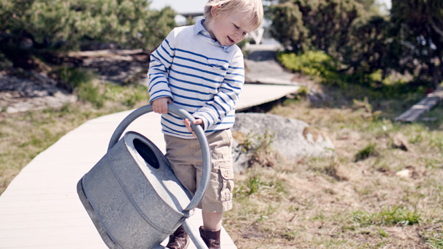 A kid with a watering can outside summertime. 