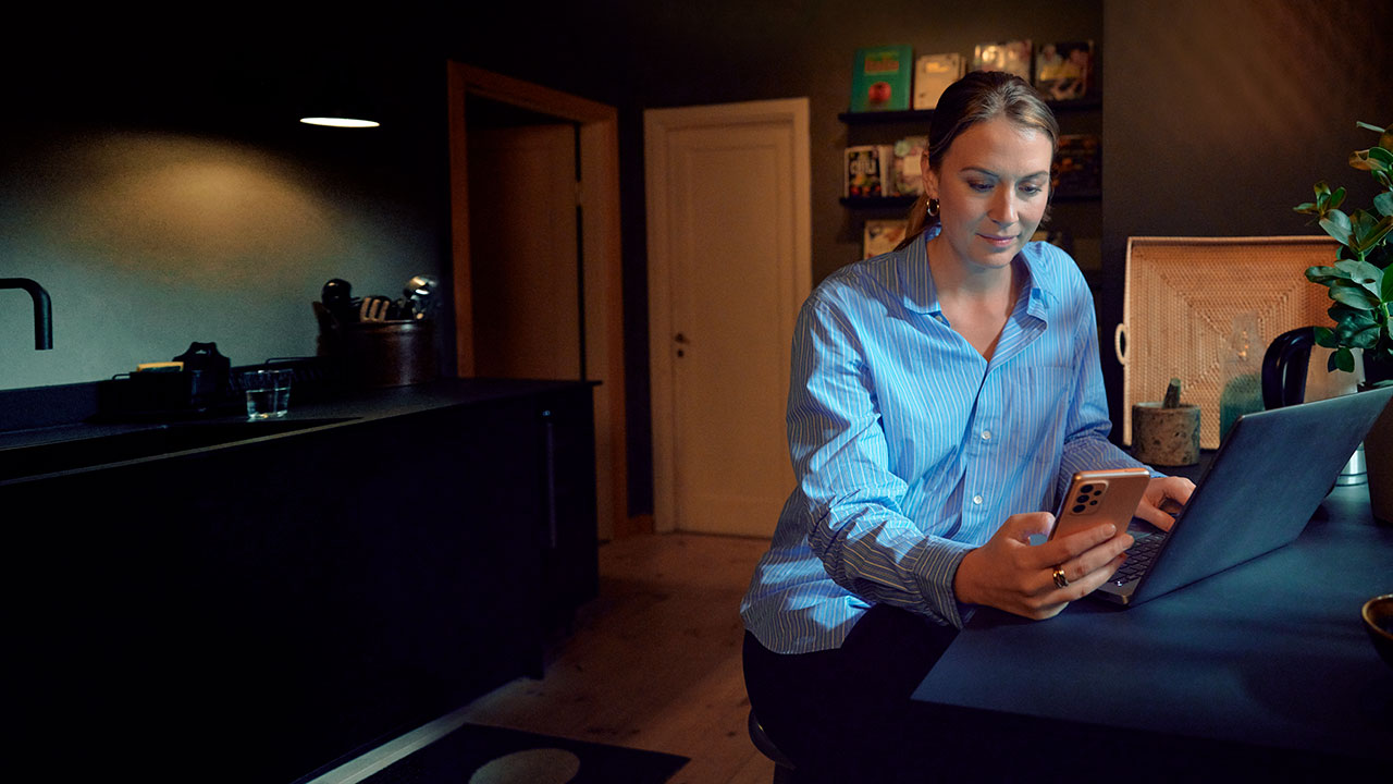 Woman in kitchen with computer and mobile.