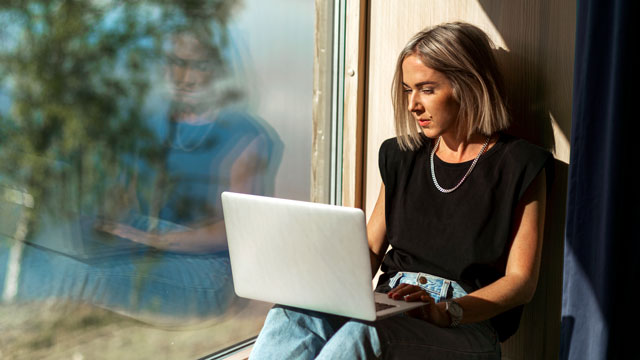 Woman working on laptop close to window 